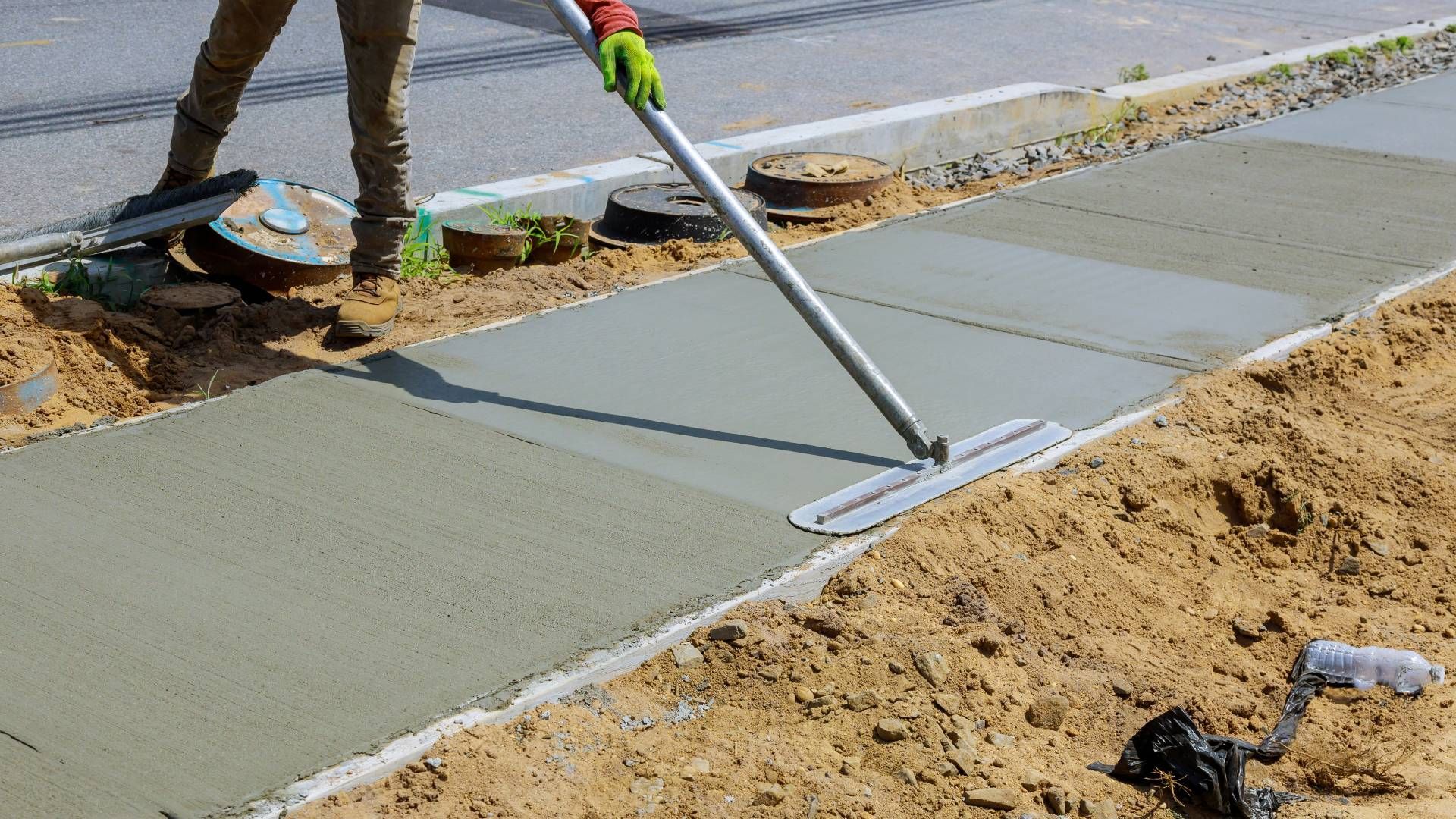 A man is using a broom to spread concrete on a sidewalk.