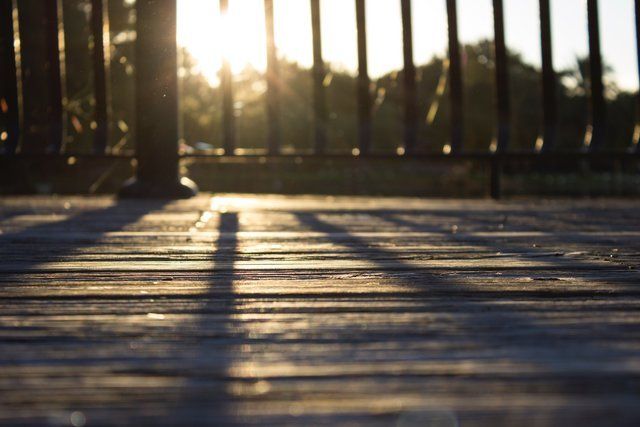 The sun is shining through the bars of a fence on a wooden deck.
