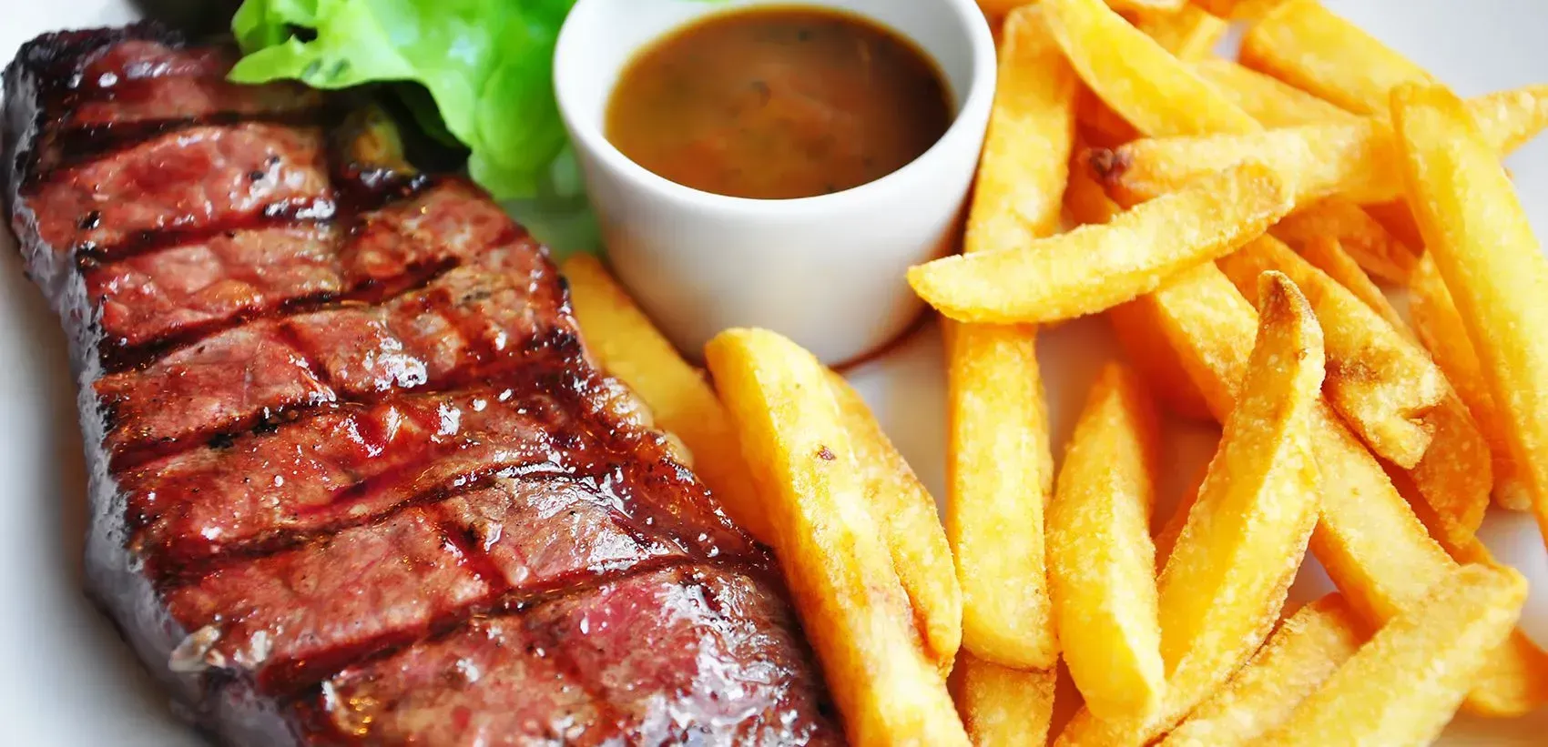 Grilled steak with french fries and gravy, presented on a white plate.
