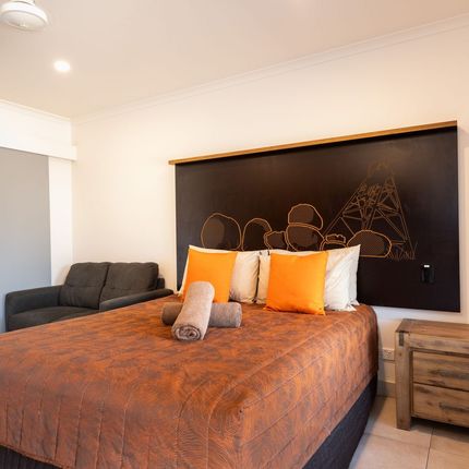 Bedroom with a large bed, orange bedding, and pillows. A small couch sits to the left. A wooden nightstand is on the right.