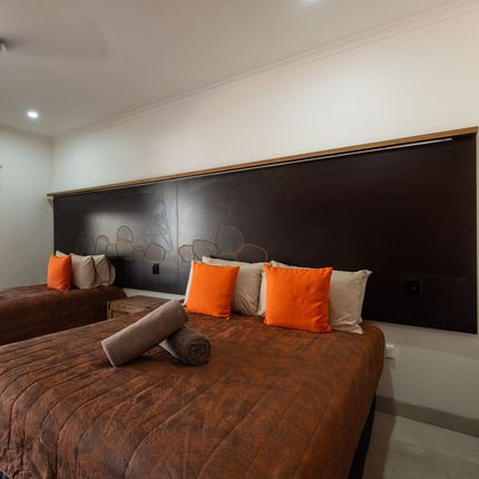 Two beds in a room with brown bedding and orange pillows. A large dark headboard decorates the wall behind the beds.