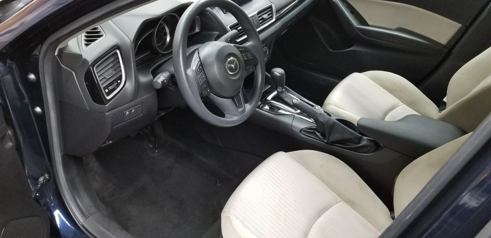 Interior of a Mazda car. Beige seats, black dashboard and steering wheel.