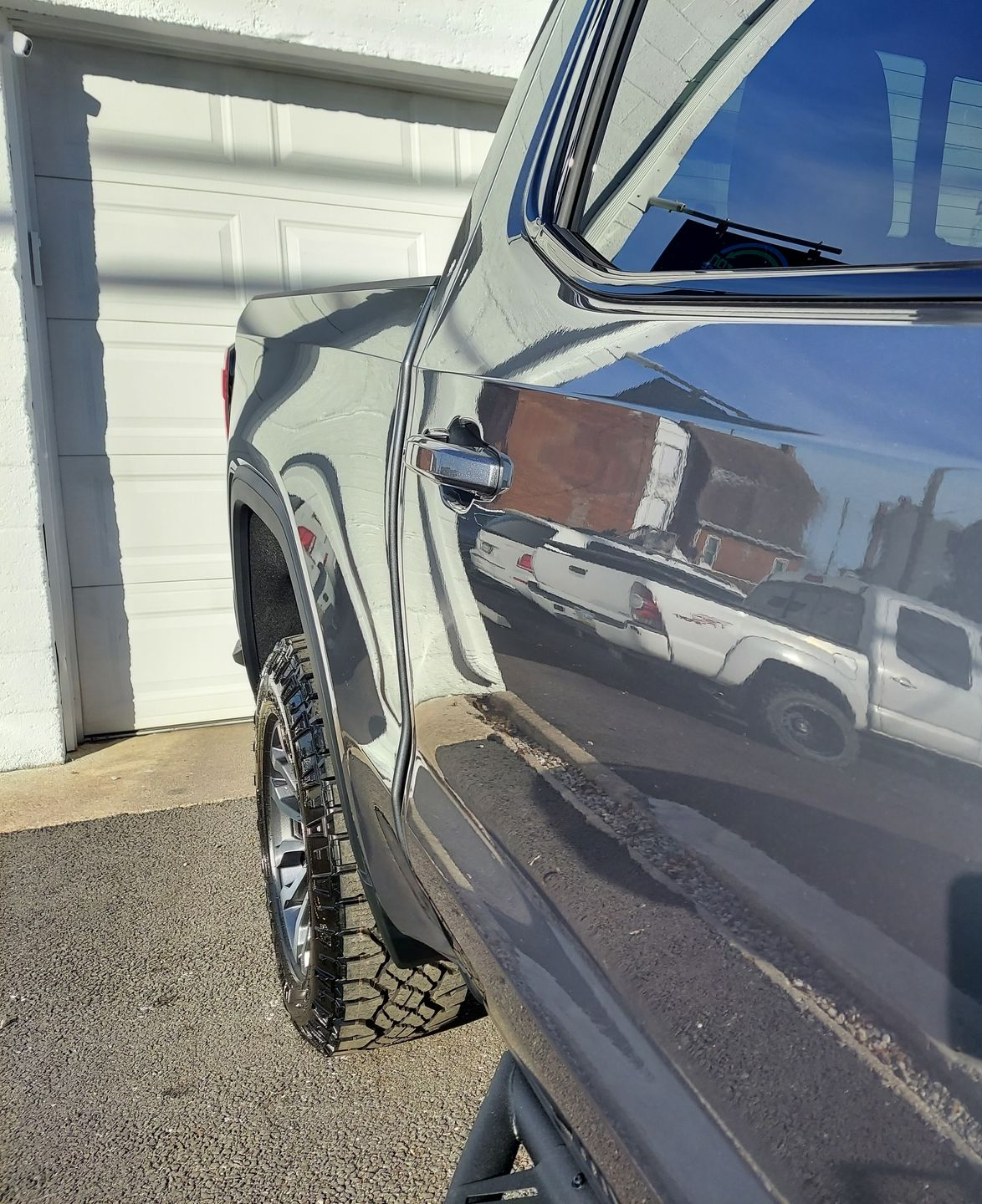 Gray pickup truck side with reflections of a white truck, garage, and setting sun.