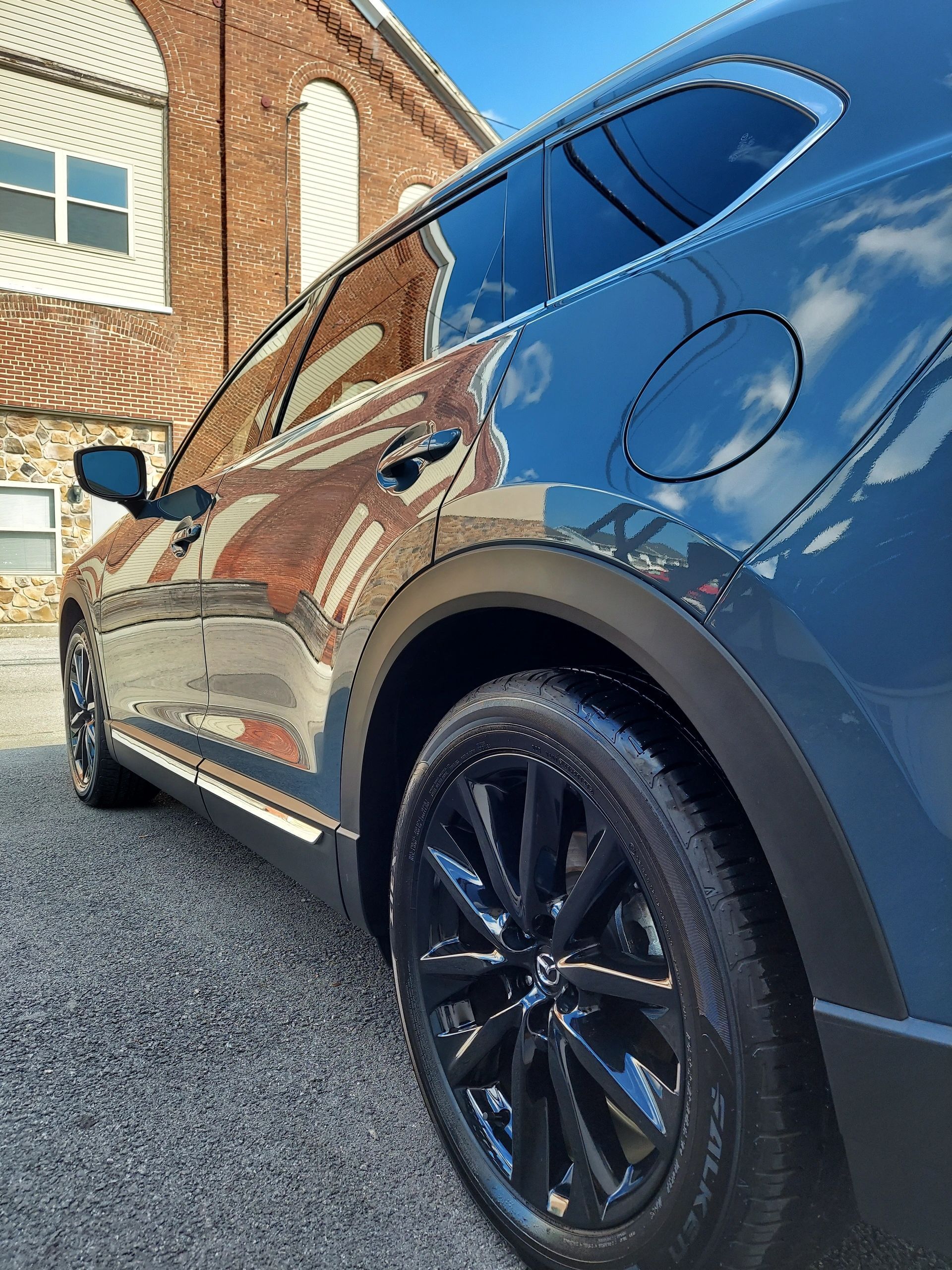 Dark SUV parked in front of a brick building, glossy black wheels and tinted windows reflect sky.