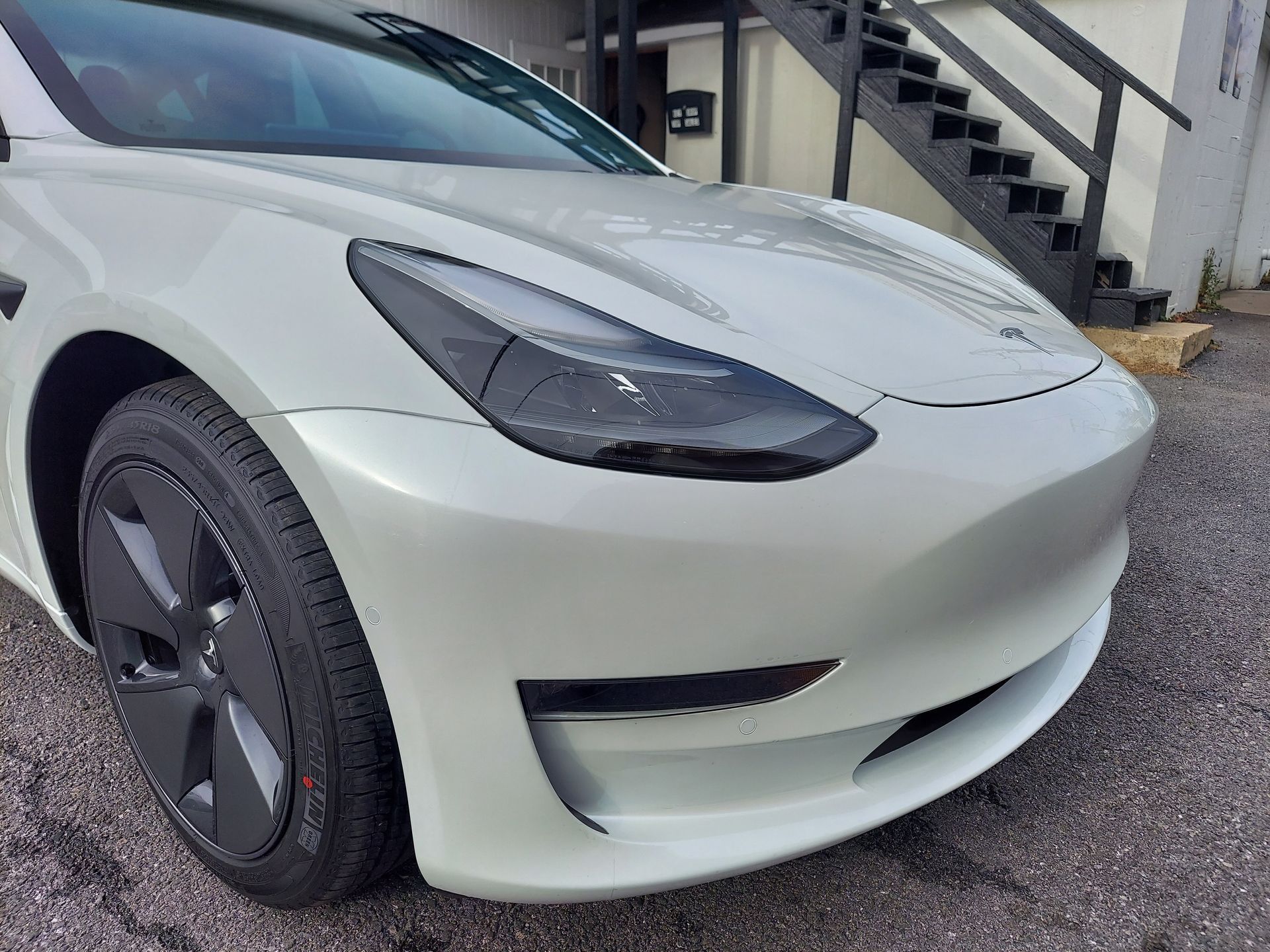 White Tesla electric car, front view, parked near a building with stairs.