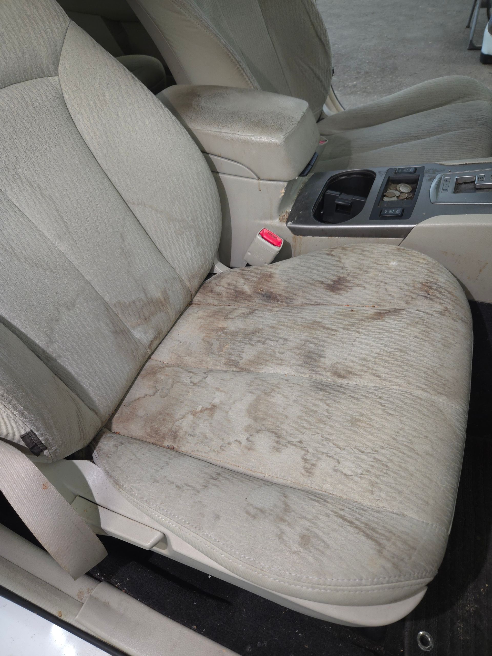 Beige car seat heavily stained with dark brown dirt and discoloration.