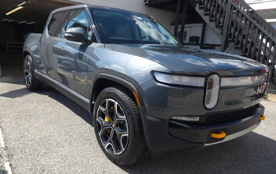 Gray Rivian electric pickup truck parked outdoors, with black and yellow accents.