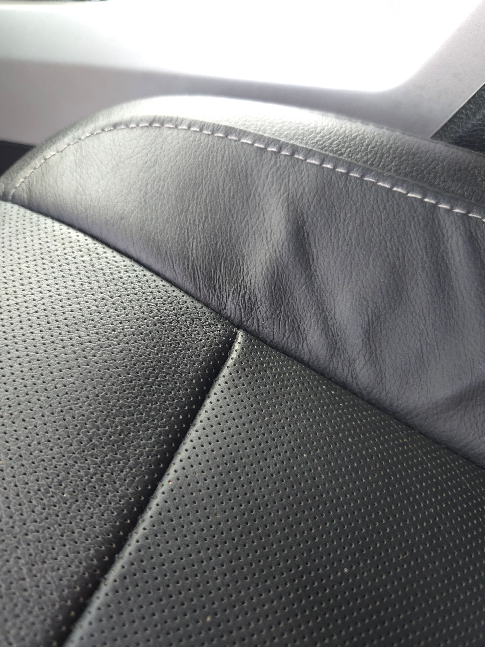 A hand wiping a white car's front grill and hood with a gray cloth.