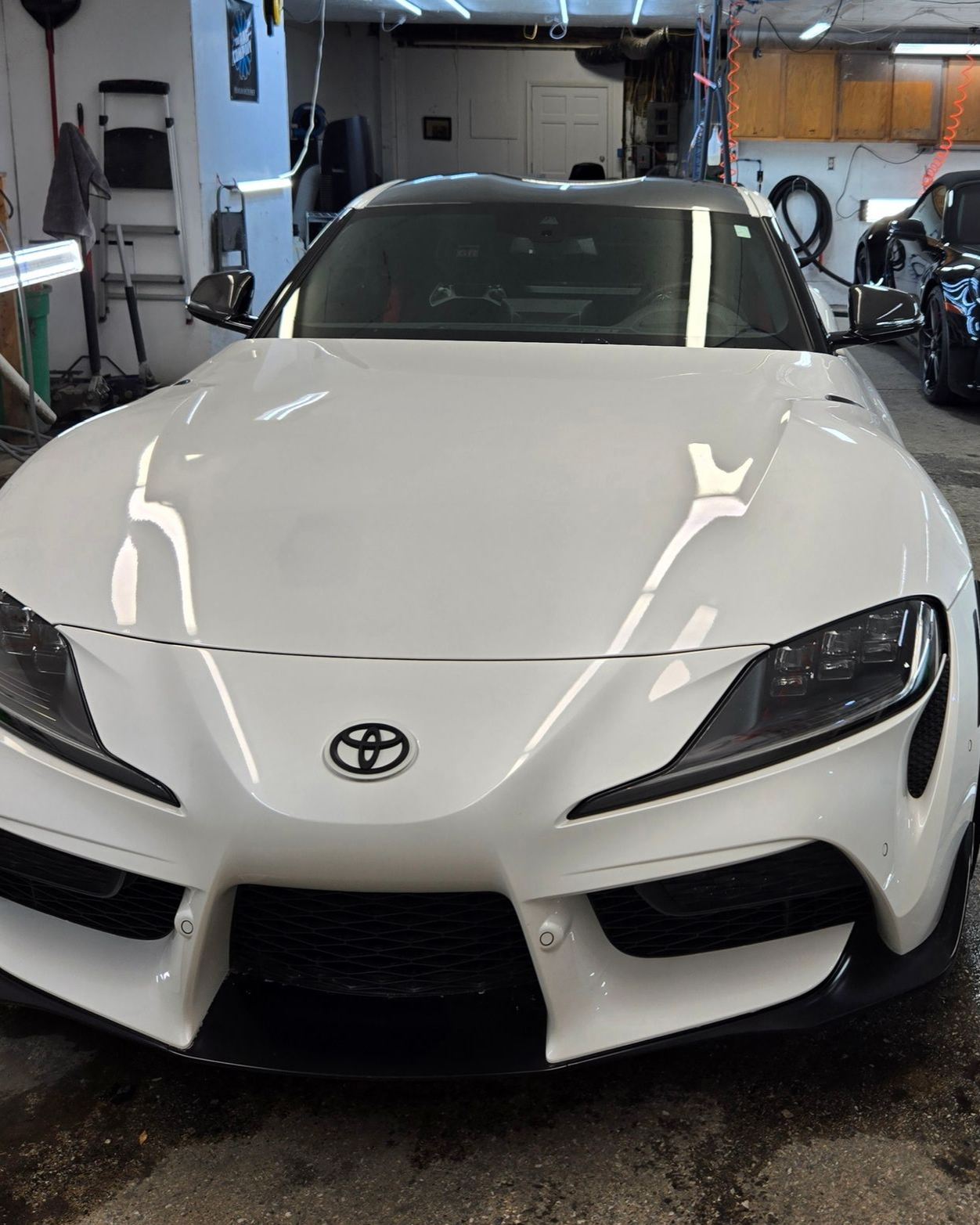 White Toyota Supra sports car in a garage with black trim, Toyota logo on the front.