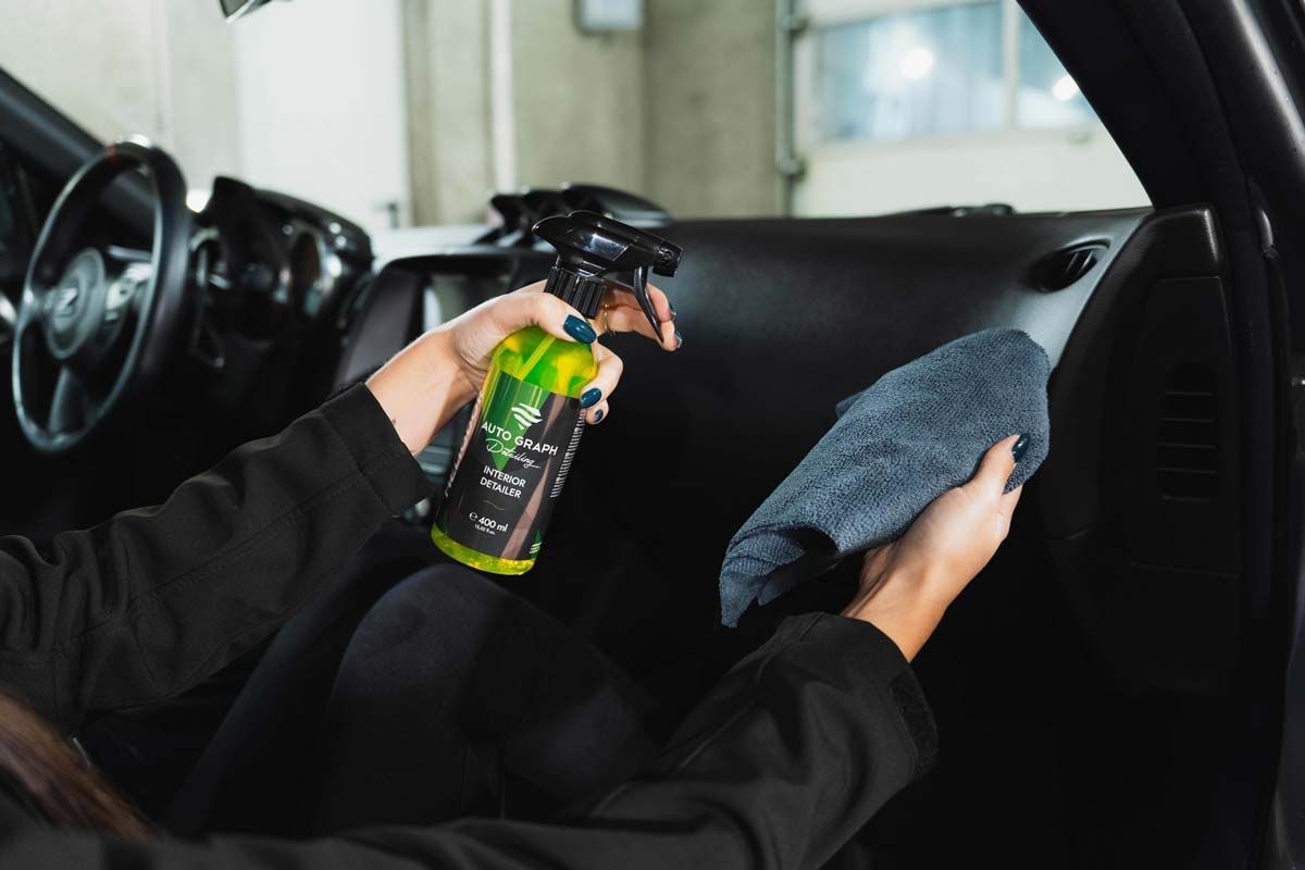 Person cleaning a car dashboard with spray and cloth.
