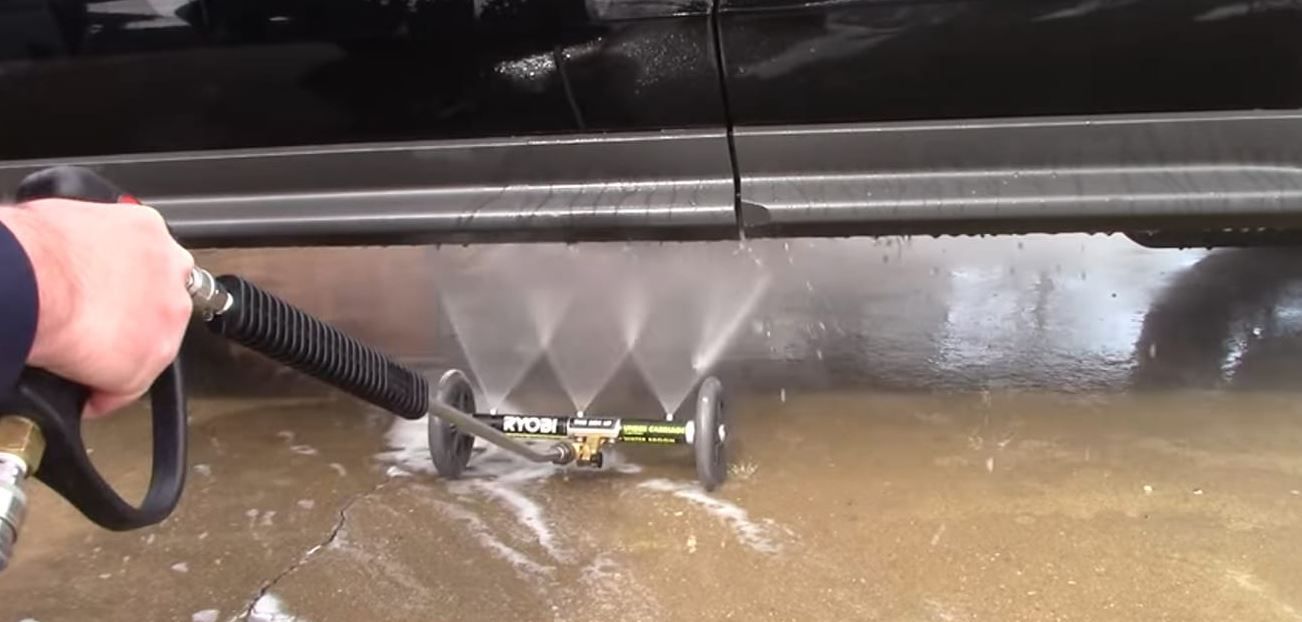 A person using a pressure washer with a wheeled undercarriage cleaner to wash the side of a black vehicle.