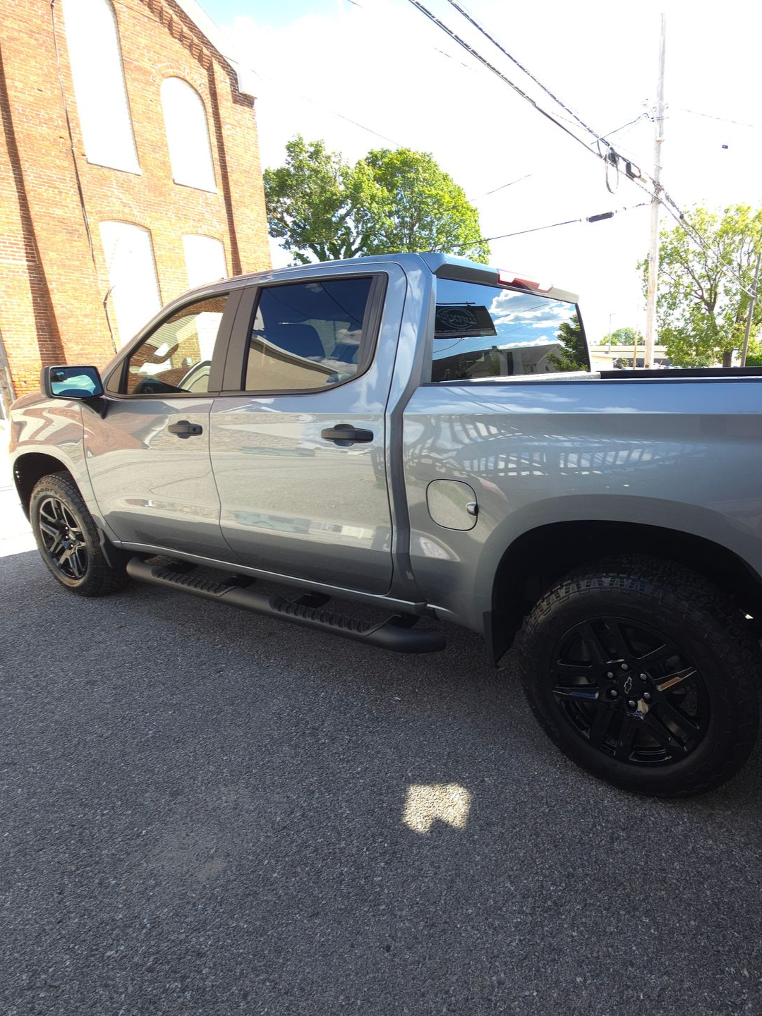 Gray pickup truck parked on asphalt next to a brick building, black wheels and running boards.