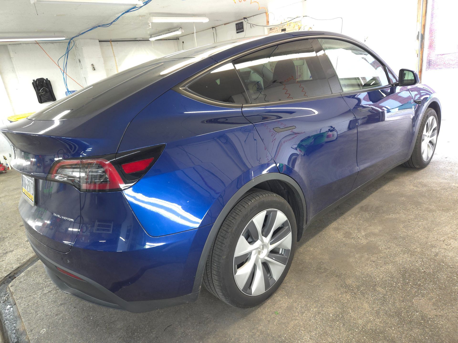 Blue Tesla Model Y, side view, parked inside, shiny paint.