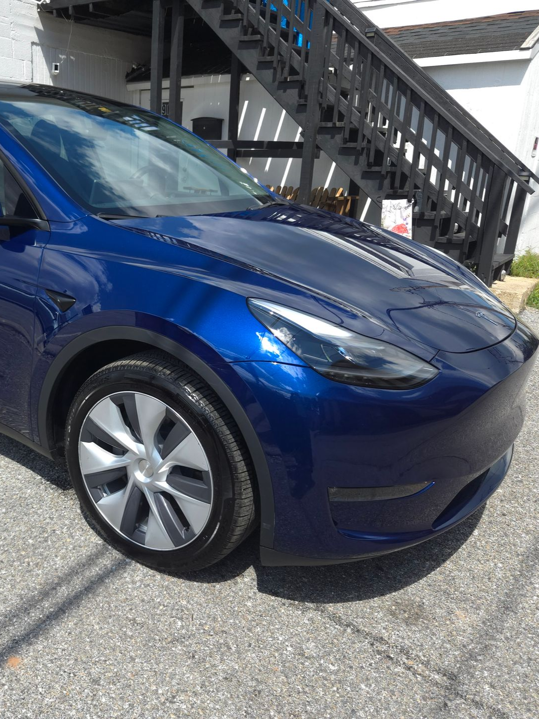 Blue Tesla Y model car parked outside a building with black stairs.