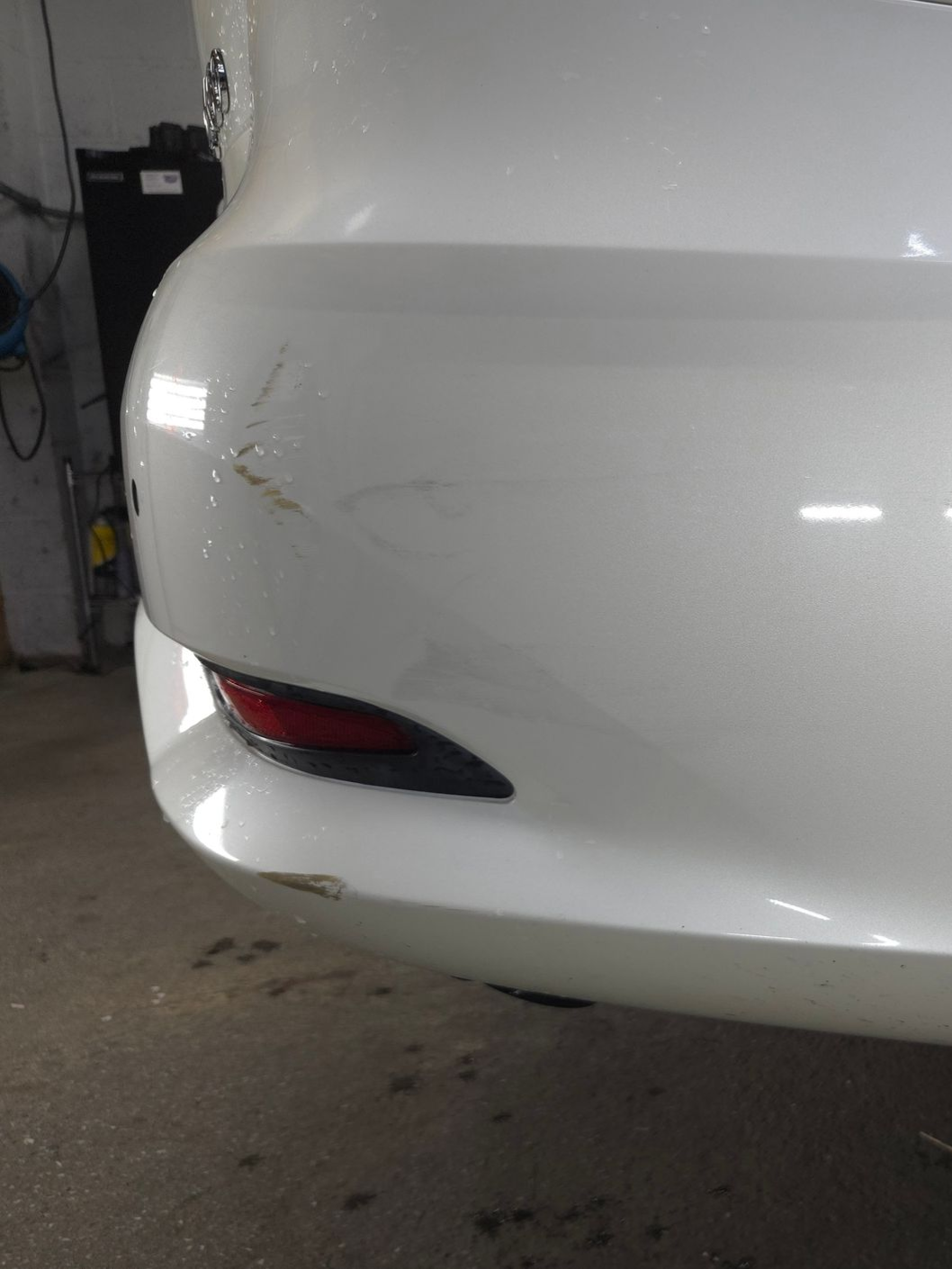 White car's rear bumper with scratches and a dent near the taillight.