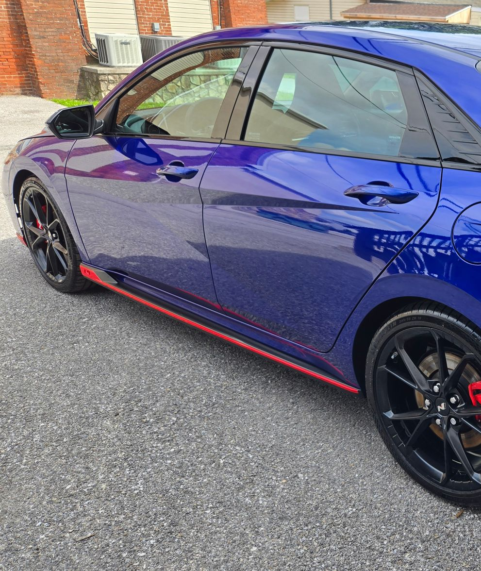 Blue car parked on a gravel driveway, featuring black wheels with red accents and a red trim.