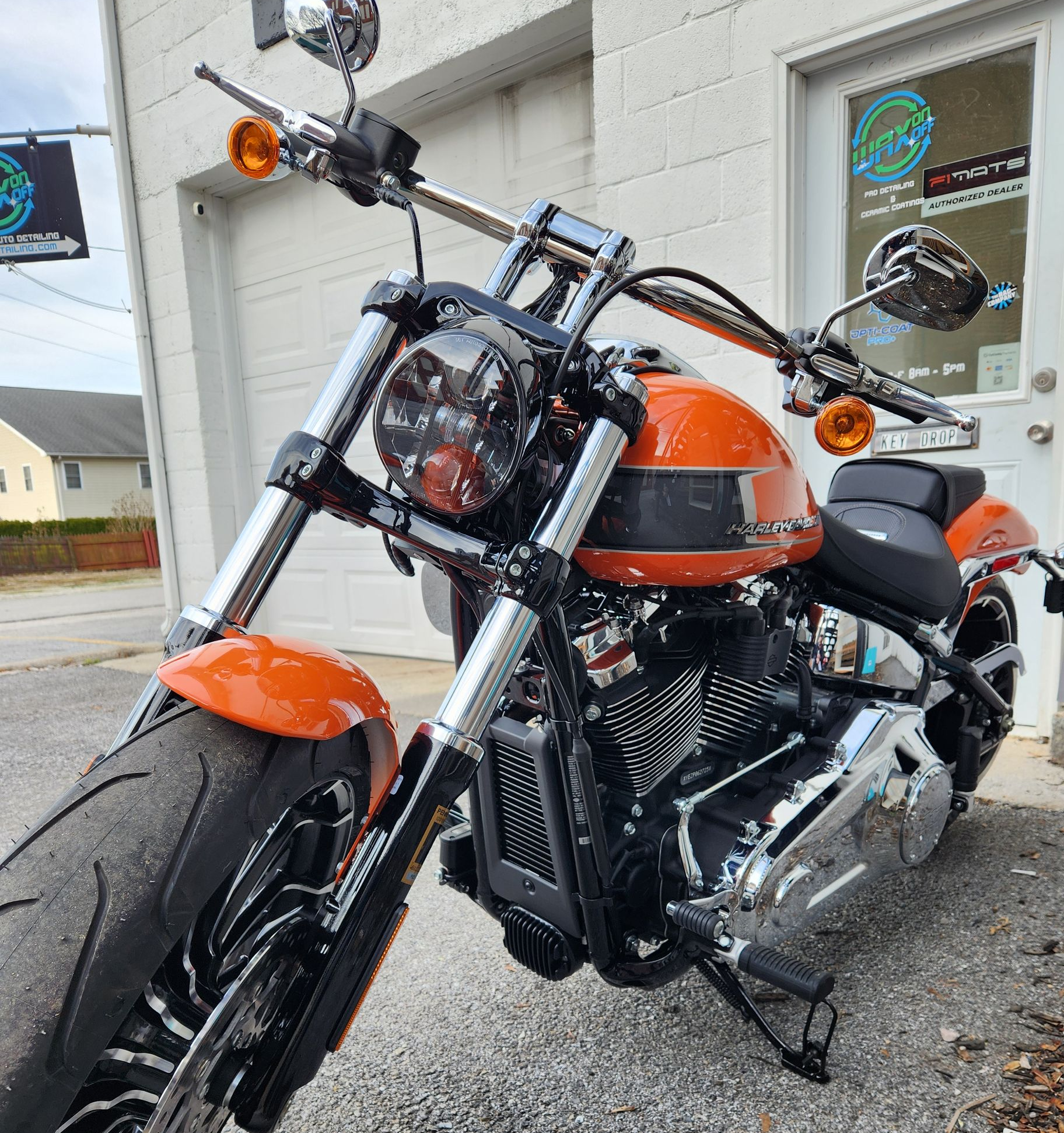 Orange Harley-Davidson motorcycle parked outside a white building. Chrome accents, black seat, and clear skies.