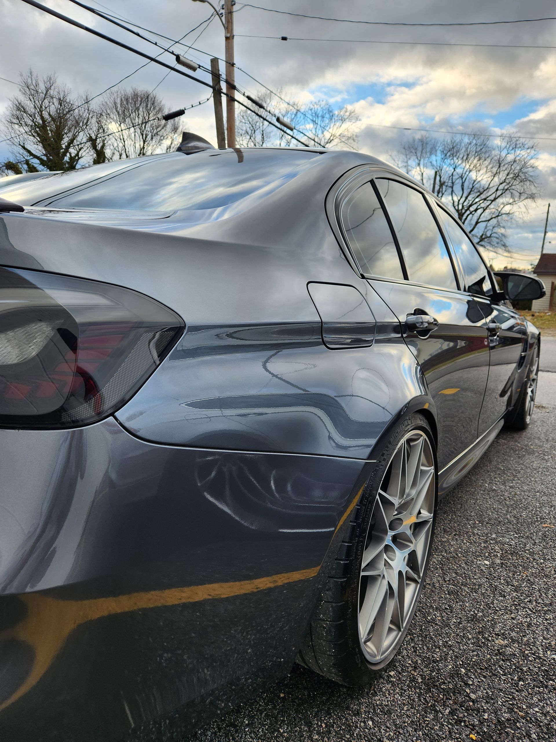 Dark gray car parked on the street, showcasing the rear quarter panel and alloy wheels.