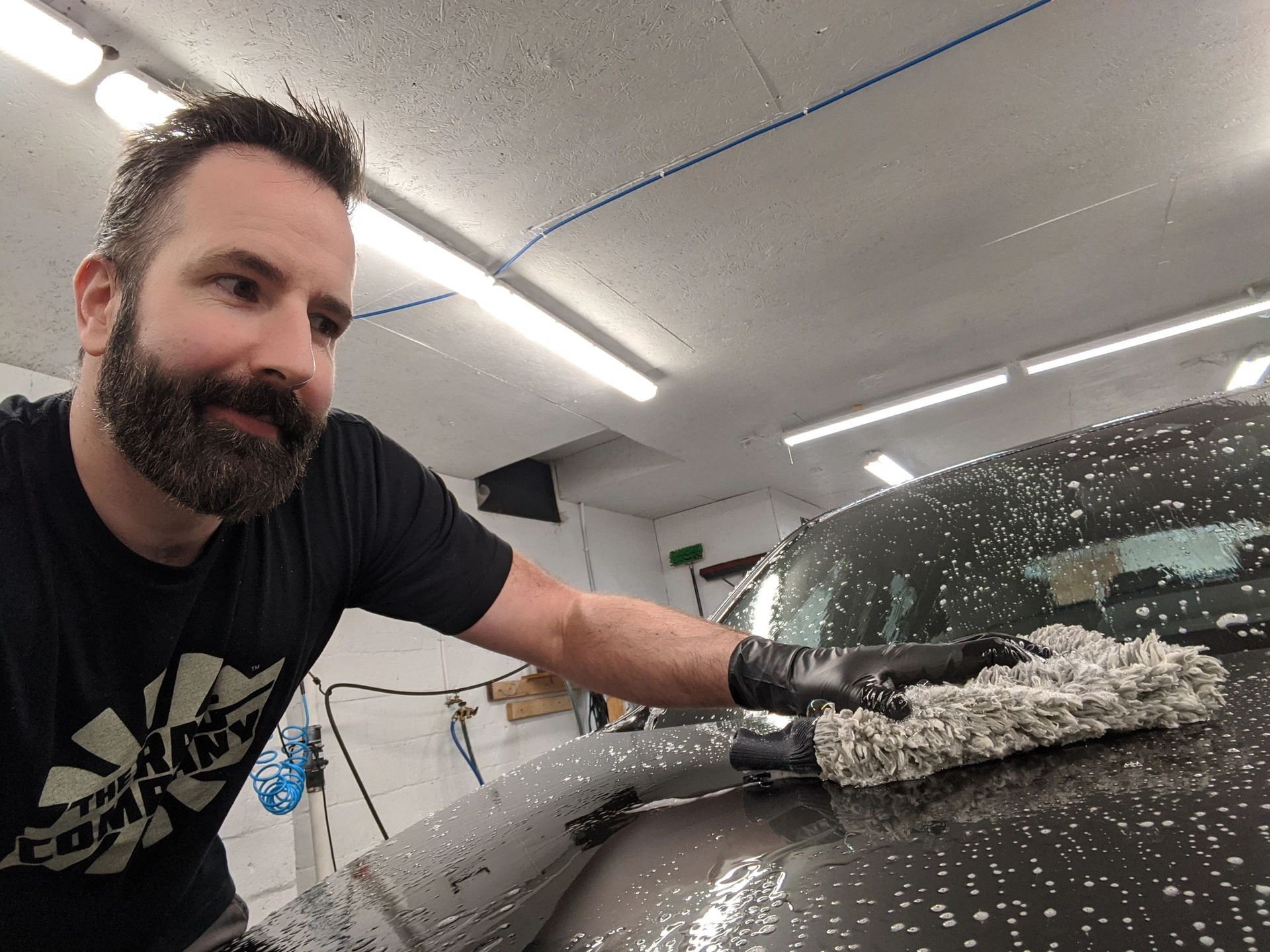 Man washing a car with soapy mitt; garage setting.