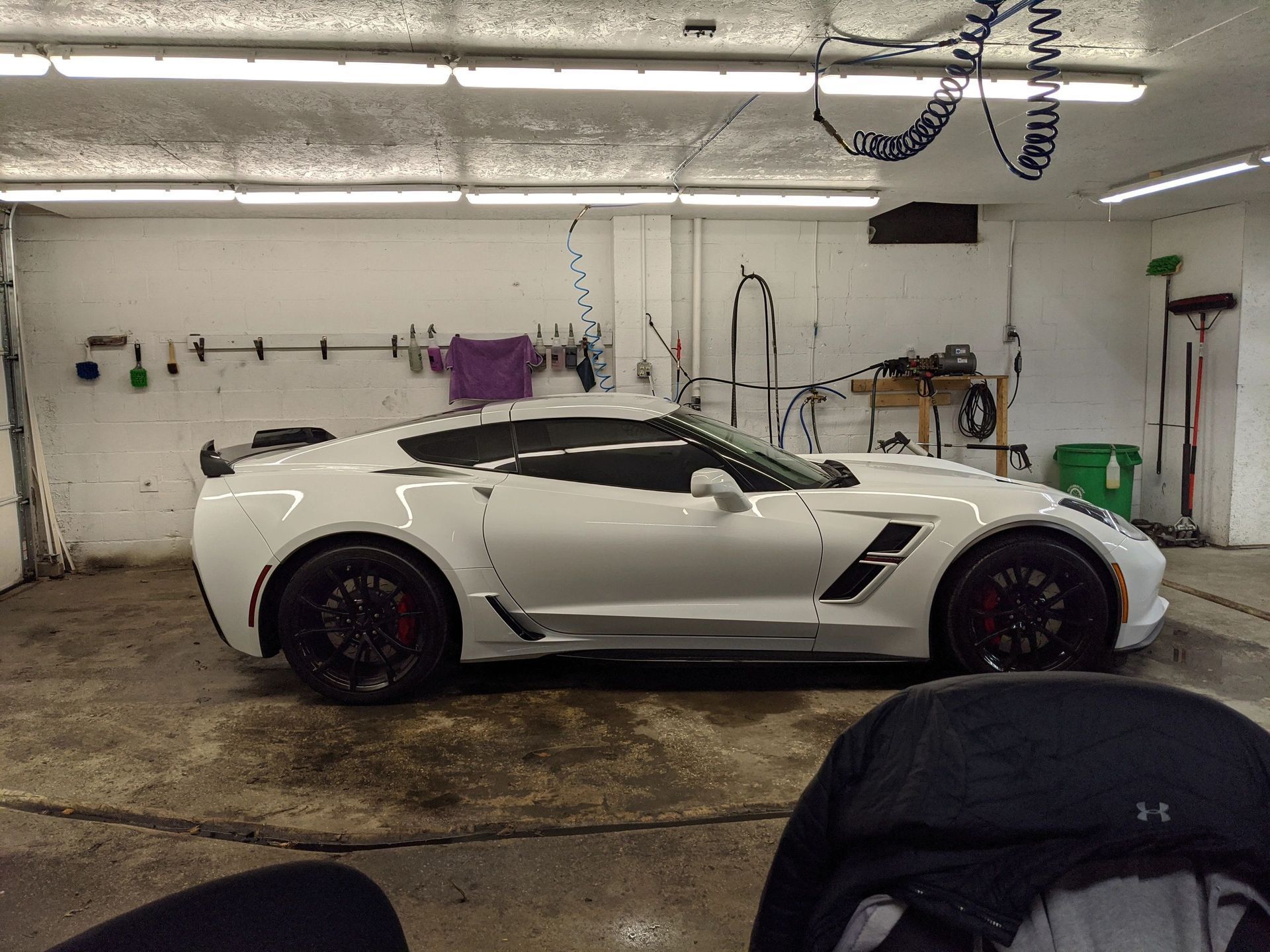 White Corvette inside a car wash bay, with dark tinted windows and black wheels.