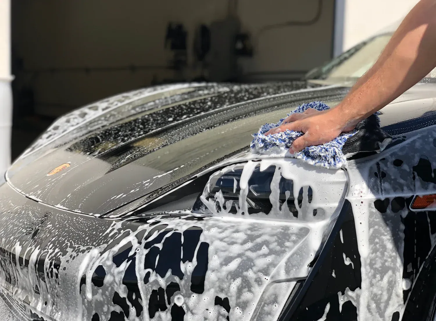 Person washing a black car with a soapy washcloth.