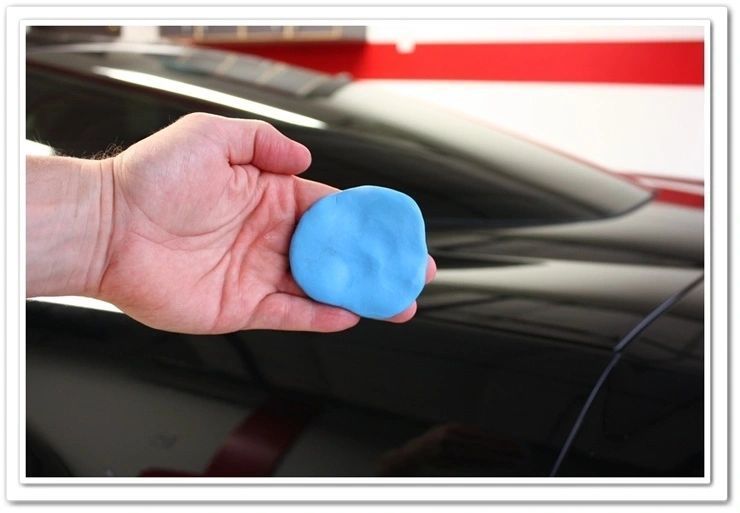 Hand holding a blue detailing clay, cleaning a black car's paint.