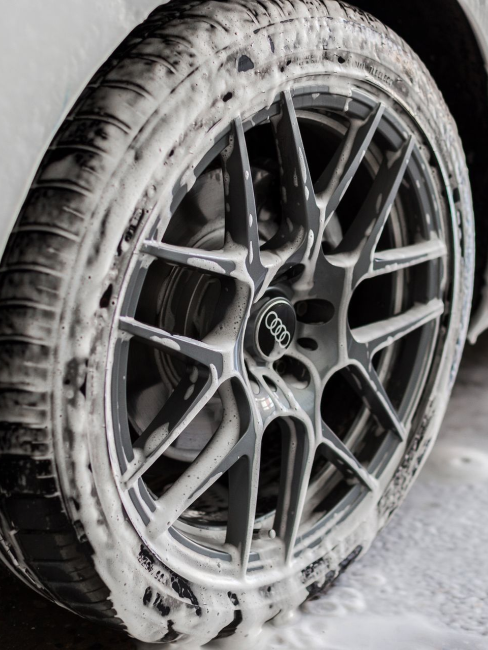 Car wheel covered in white foam, being washed.