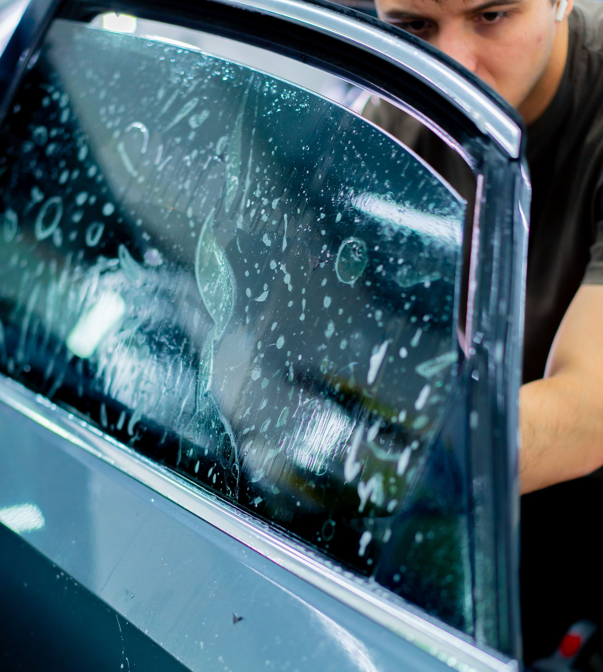 Person applying window tint to a car window, using spray and tools.