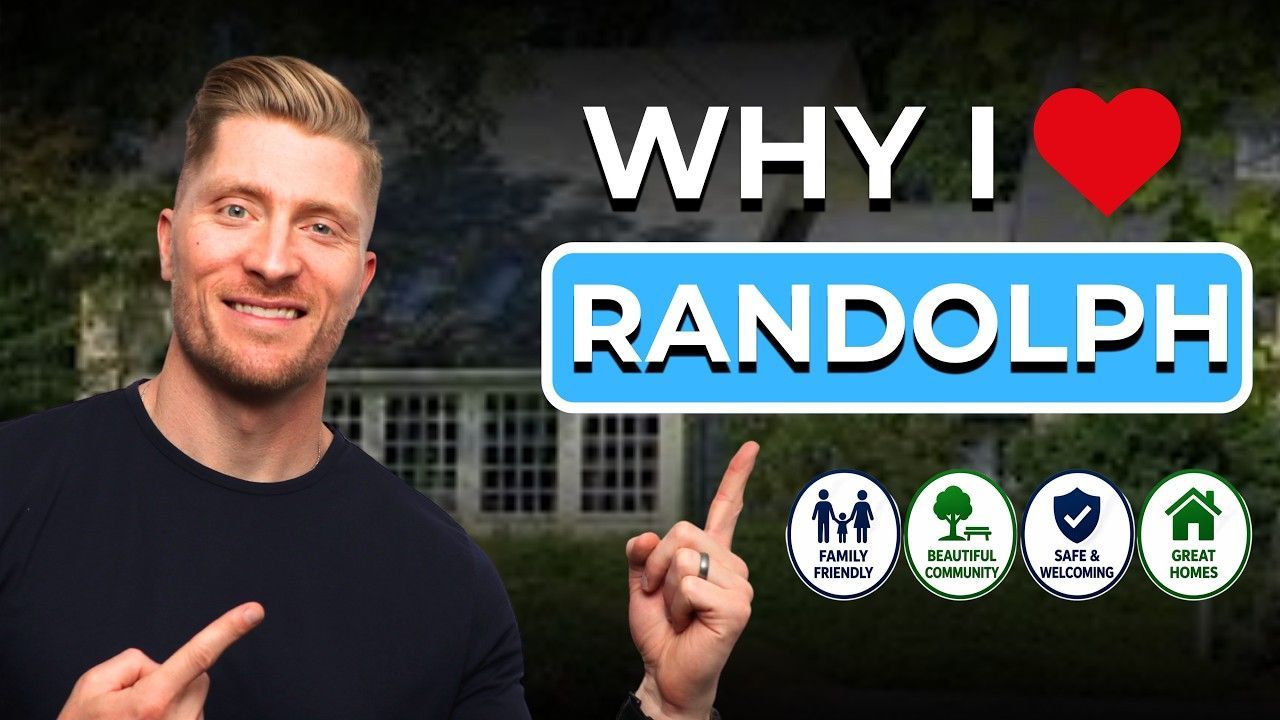 Man pointing at “Why I ♥ Randolph” sign, with town seal logos on a green lawn background