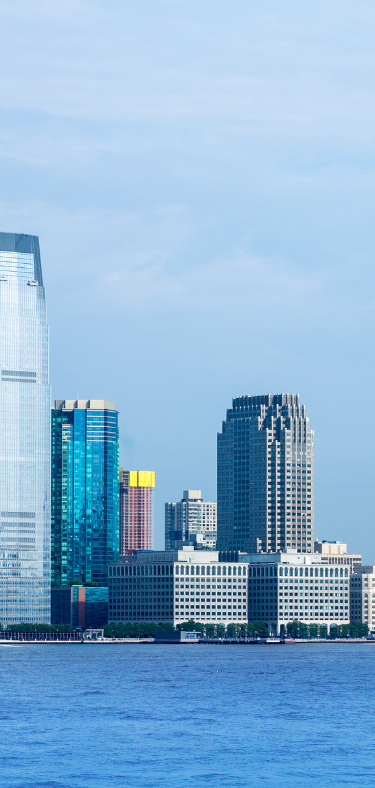 Skyline of Jersey City, New Jersey, with buildings of various heights along the waterfront. Blue water in the foreground.