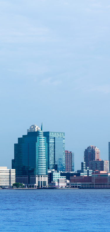 City skyline of tall buildings along a body of water under a blue sky.