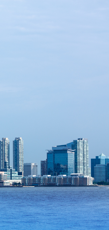 Skyline of modern buildings along a body of water under a blue sky.