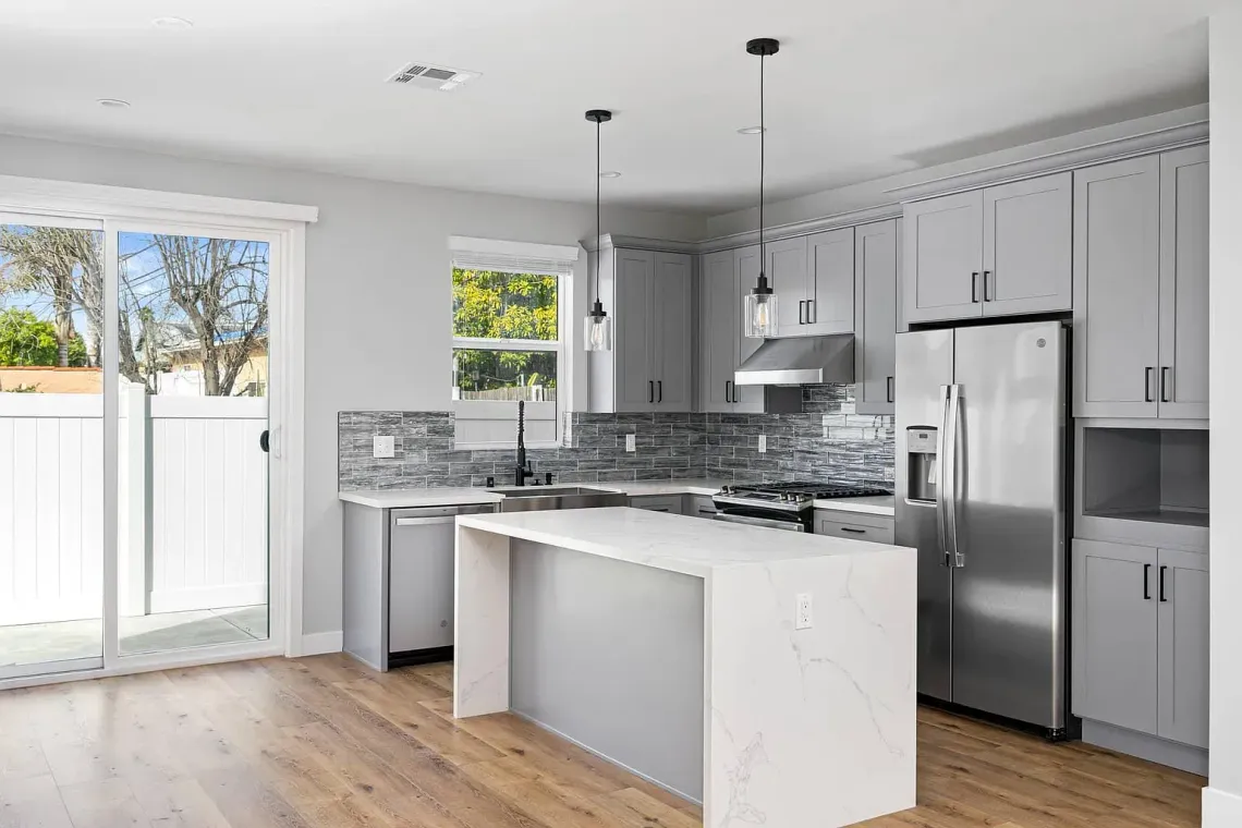 Sliding glass doors allow plenty of sunshine into this full kitchen inside an accessory dwelling unit (ADU) backyard home, featuring plenty of space, an island, and modern all-electric appliances. 