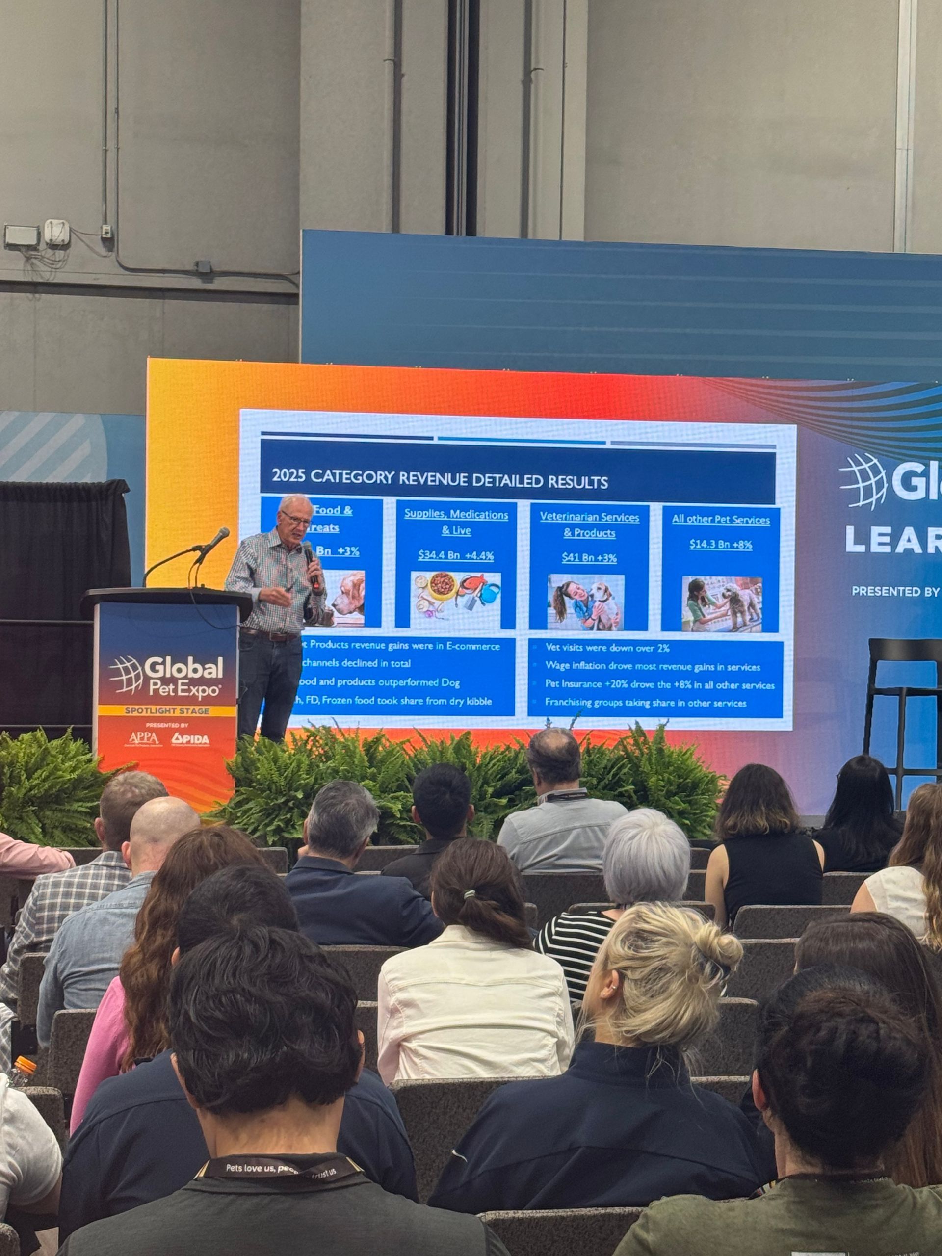 Four people stand side-by-side indoors, smiling toward the camera. They wear casual clothing including green jackets.