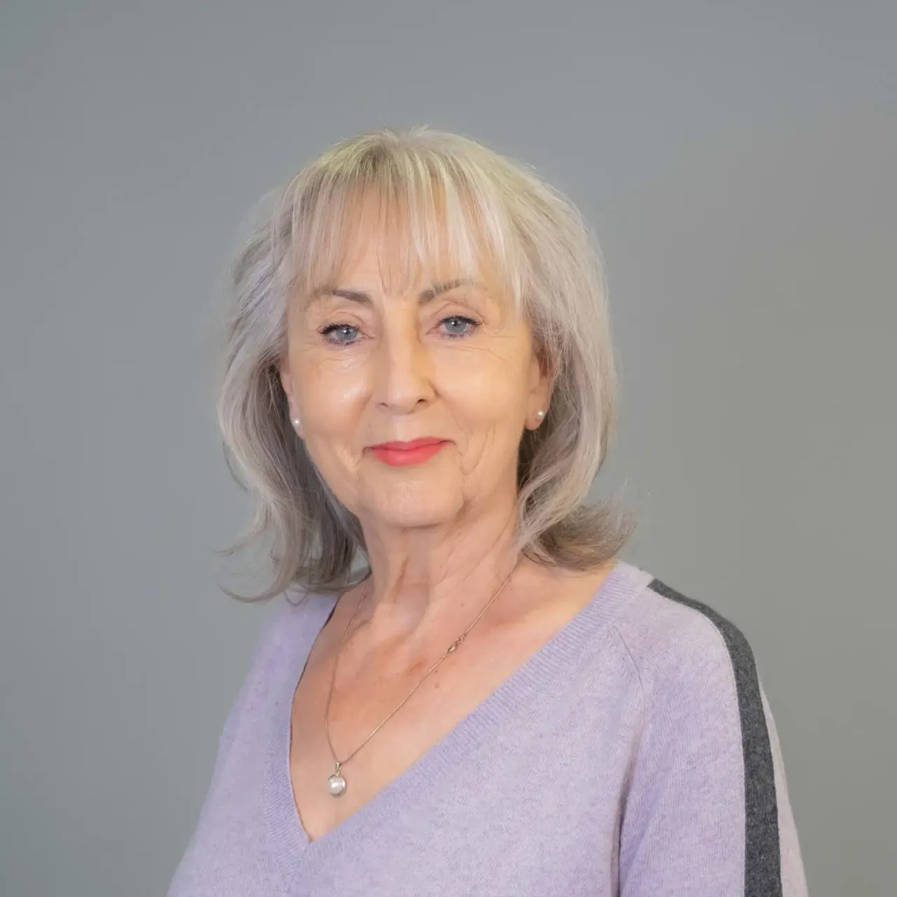 Woman with gray hair and a light purple sweater smiles at the camera.