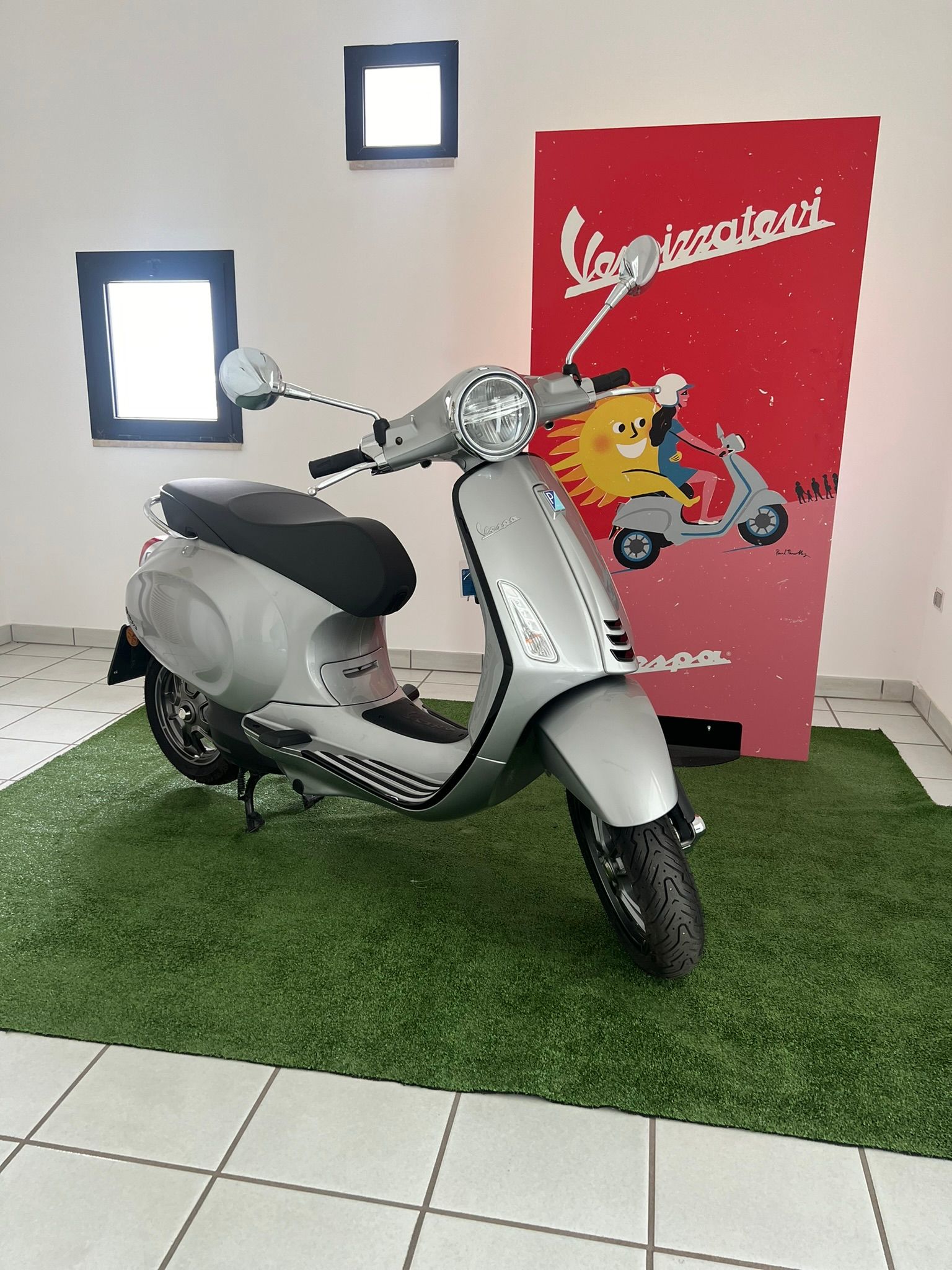 Uno scooter Vespa è parcheggiato in una stanza accanto a un cartello che con il logo della Vespa.