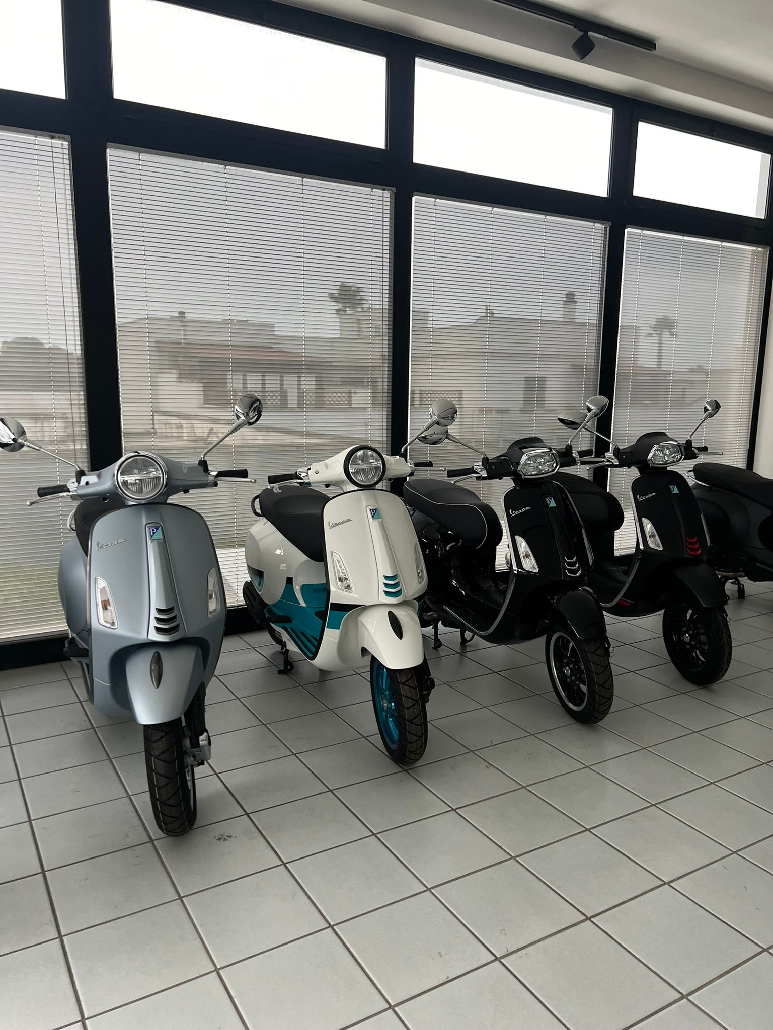 Tre scooter sono parcheggiati in una stanza davanti a una finestra.