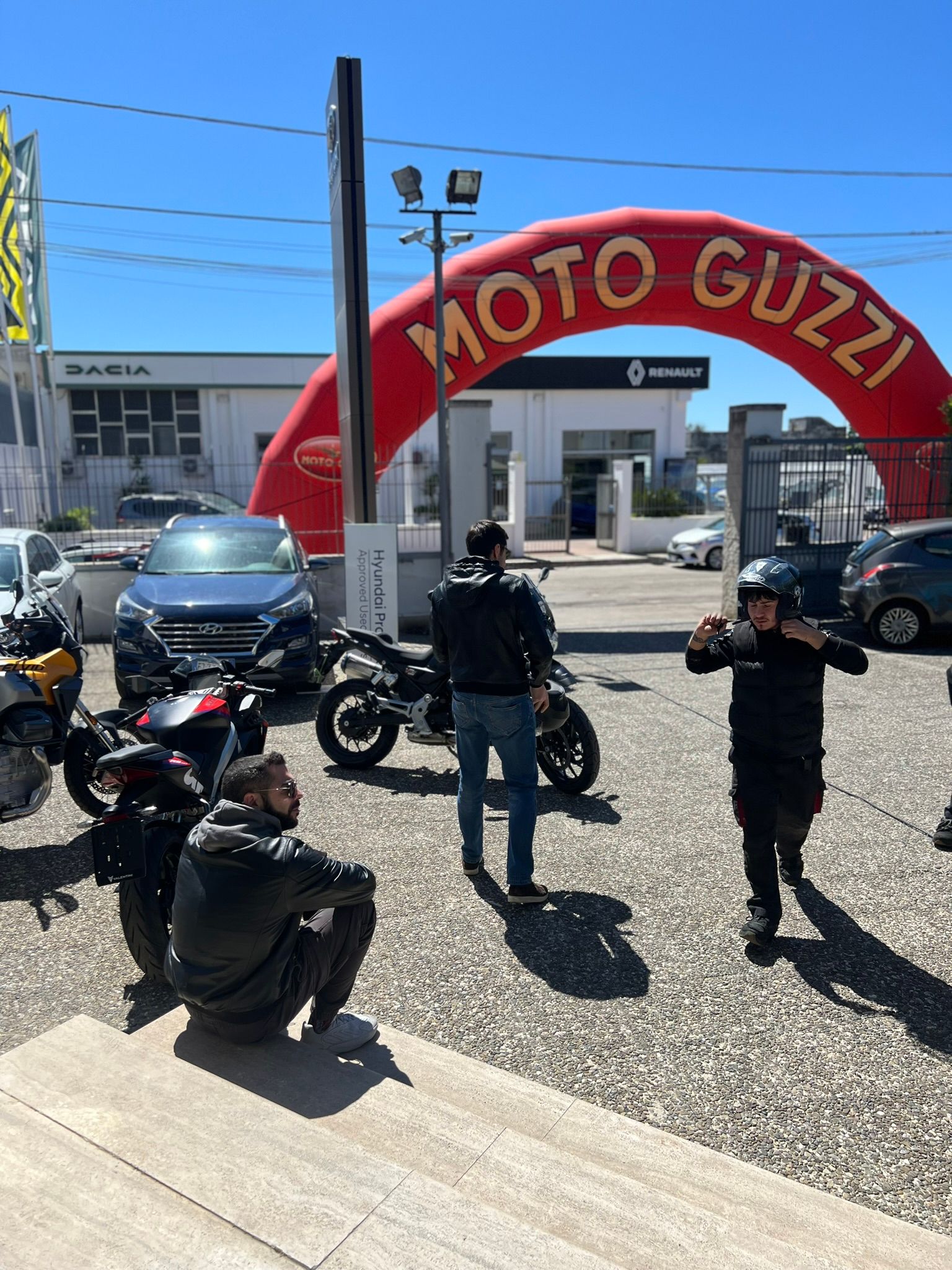 Un gruppo di persone è in piedi davanti a un cartello rosso della Moto Guzzi.