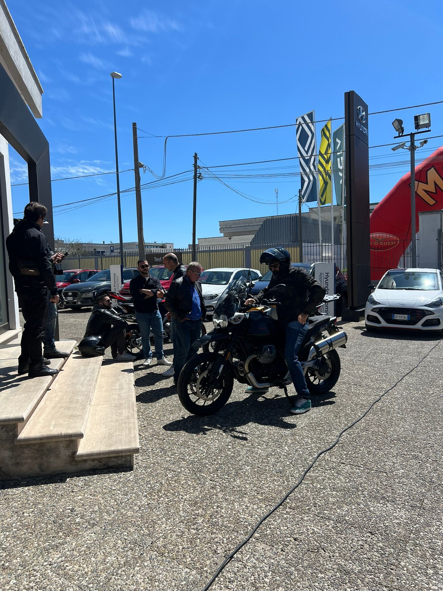 Un gruppo di persone è in piedi attorno a una moto in un parcheggio.