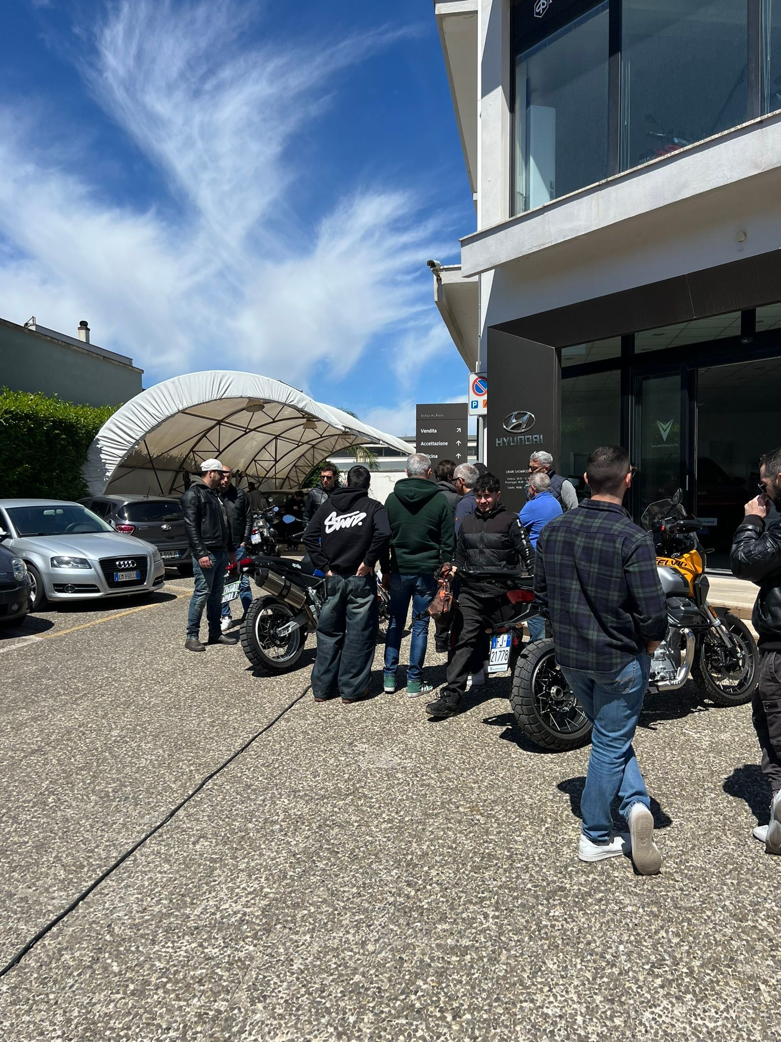 Un gruppo di persone è fermo in un parcheggio accanto a delle moto.
