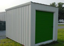 A white shed with a green door is sitting in the grass.