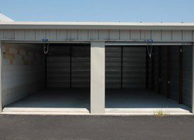 Two empty garages with their doors open on a sunny day.