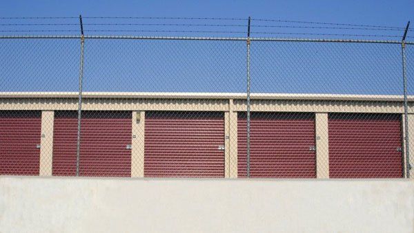 A row of red garage doors behind a chain link fence