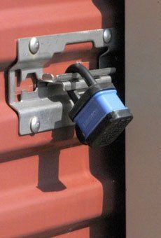 A blue padlock is secured to a red door.