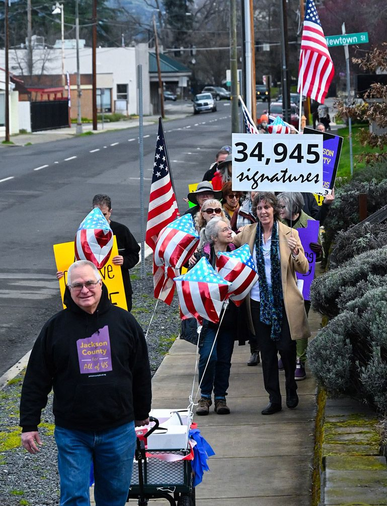 Denise Krause and volunteers march on a sidewalk, waving American flags and holding signs. 