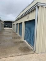 Exterior view of storage units with blue roll-up doors, beige siding, and a concrete walkway.