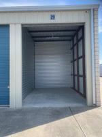 Open, empty storage unit with gray corrugated metal walls and blue door. Unit number 29.