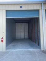 Empty storage unit with blue door, tan walls, and concrete floor.