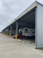 Metal storage units, covered, with vehicles parked inside. Gray, overcast sky.