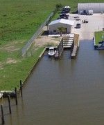 Dock with a small boat, building, and green grass next to water.